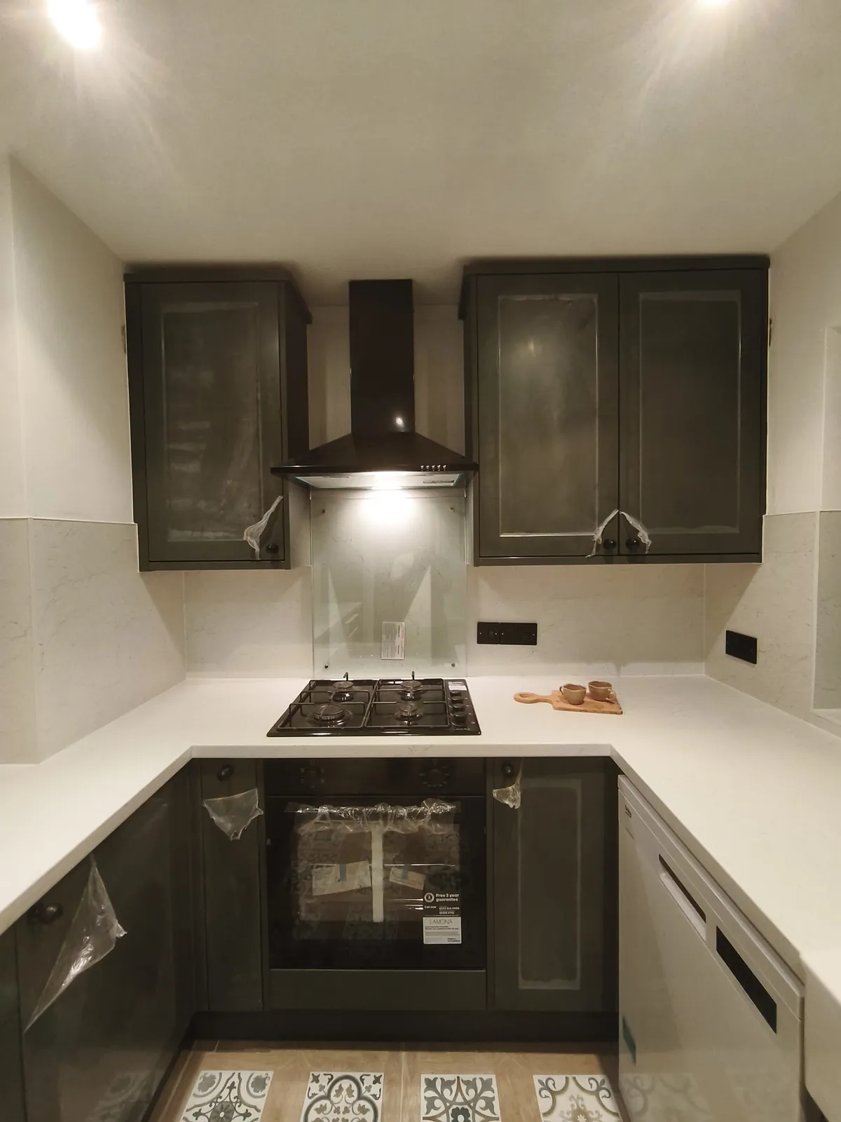 Dark green shaker kitchen with white worktops, a gas hob, a built-in oven and a chimney hood