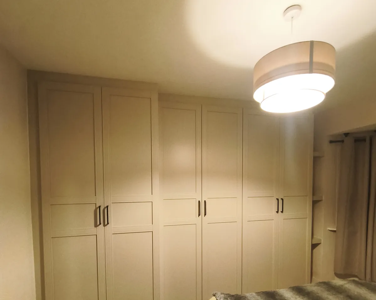 Beige shaker-door IKEA PAX wardrobes fitted across a bedroom wall, tight to the walls and closed off at the ceiling