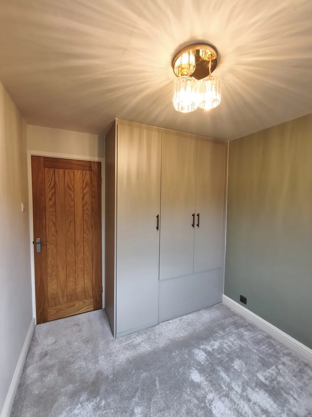 Floor-to-ceiling IKEA PAX wardrobe with flat grey doors and black bar handles, fitted into a bedroom corner beside the door