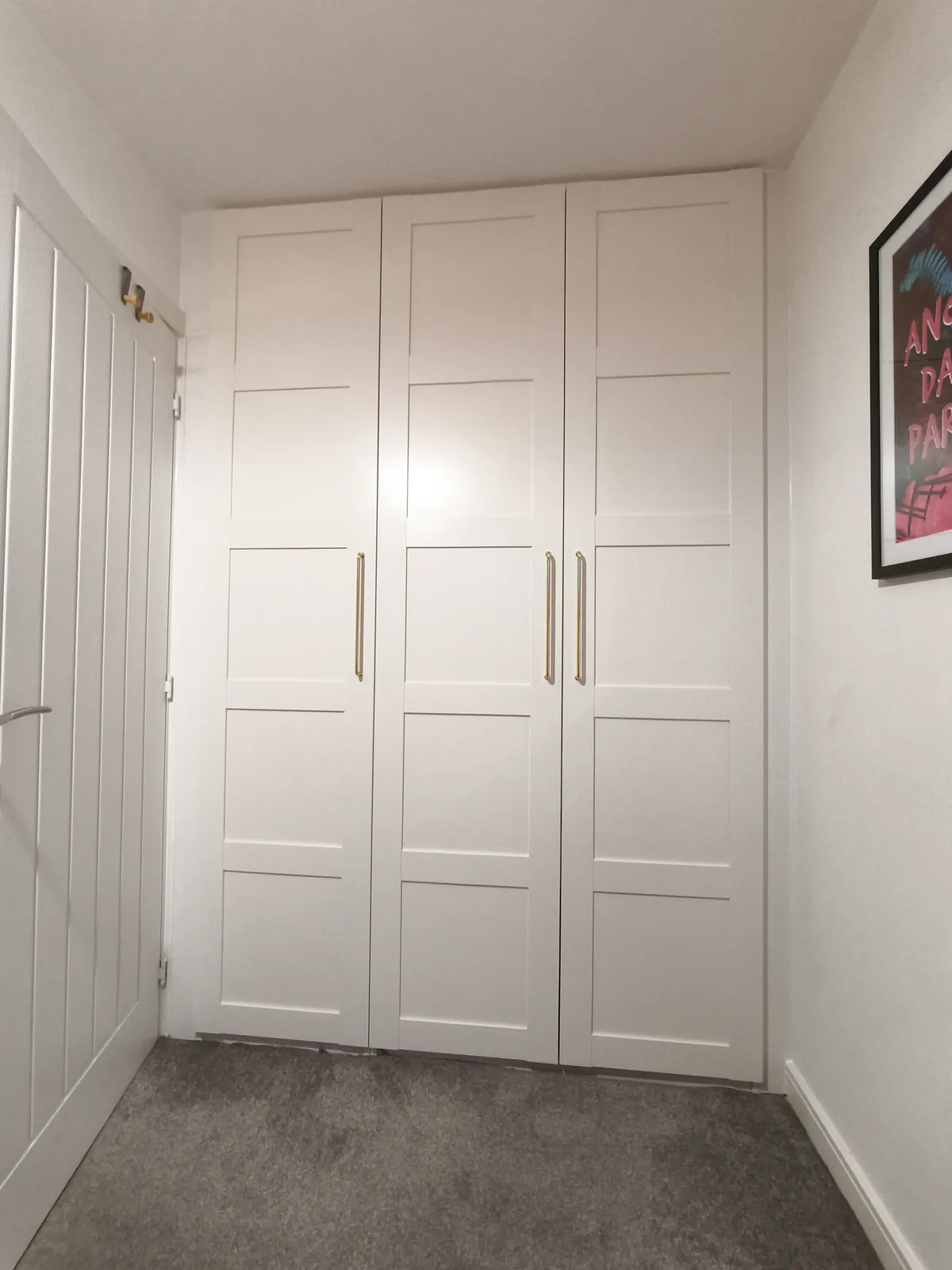 Three white shaker doors with slim bar handles on IKEA PAX wardrobes fitted into a bedroom alcove, closed off under the sloping ceiling