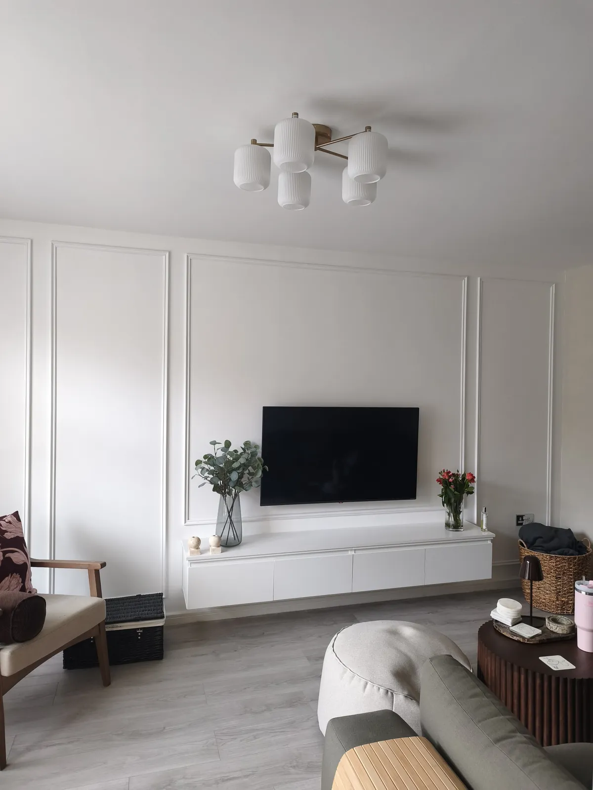 White picture-frame panelling on a lounge wall behind a wall-mounted TV and a floating white TV unit
